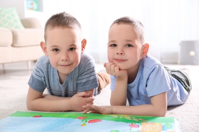 Photo of Portrait of cute twin brothers with book on floor in living room