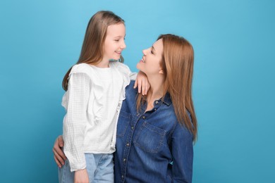 Portrait of mother and her cute daughter on light blue background