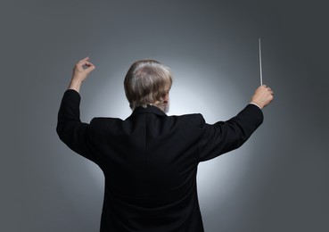 Photo of Professional conductor with baton on grey background, back view