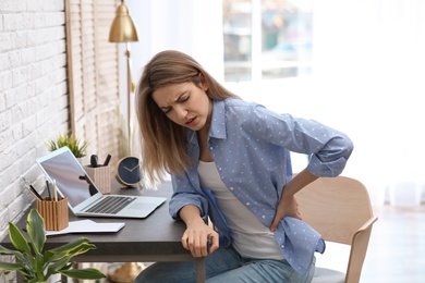 Photo of Young woman suffering from back pain in office