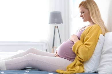 Photo of Beautiful pregnant woman resting on bed in light room. Space for text