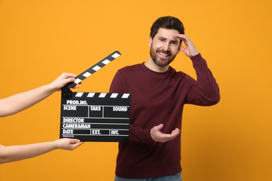 Photo of Smiling actor performing while second assistant camera holding clapperboard on orange background