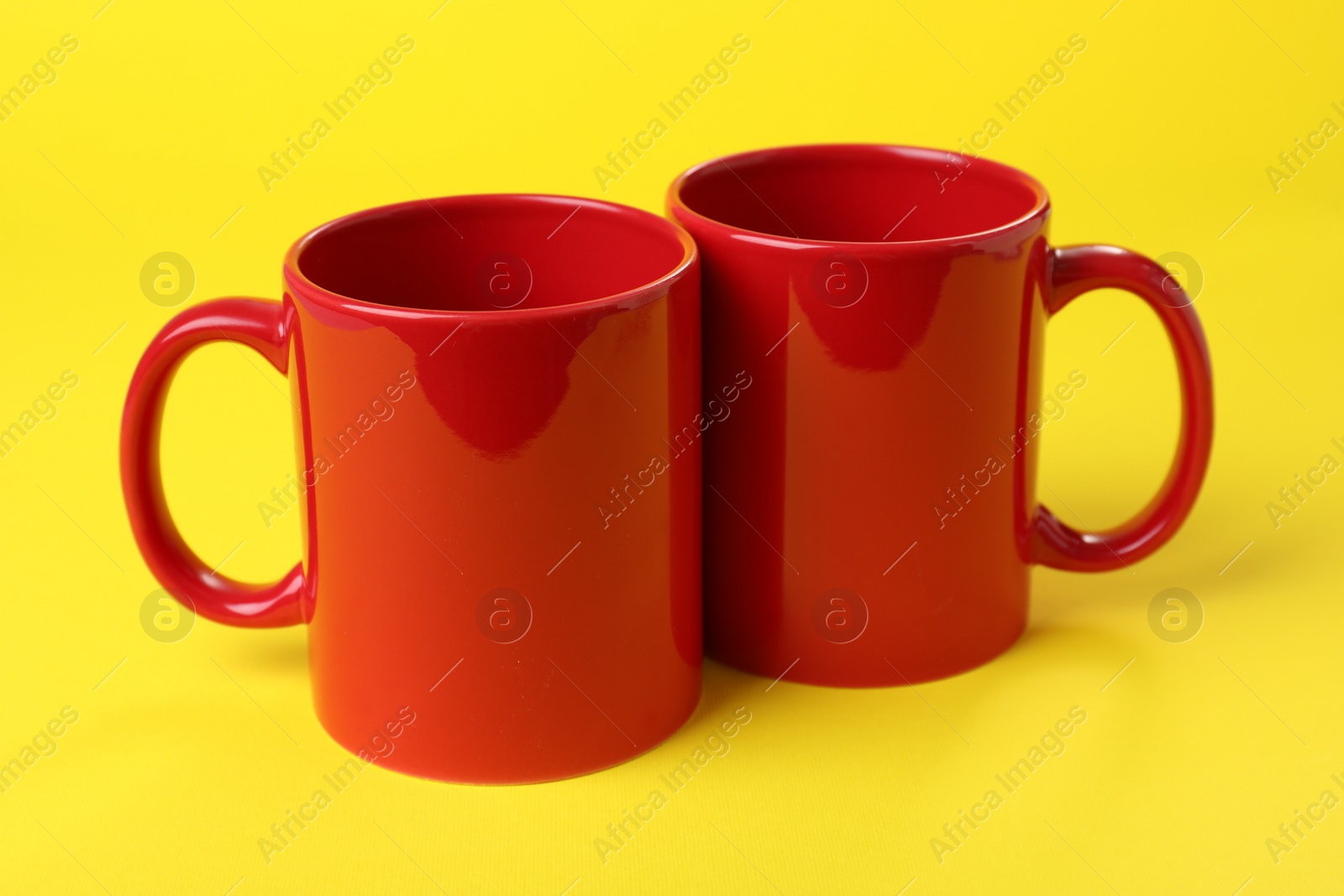 Photo of Two red ceramic mugs on yellow background