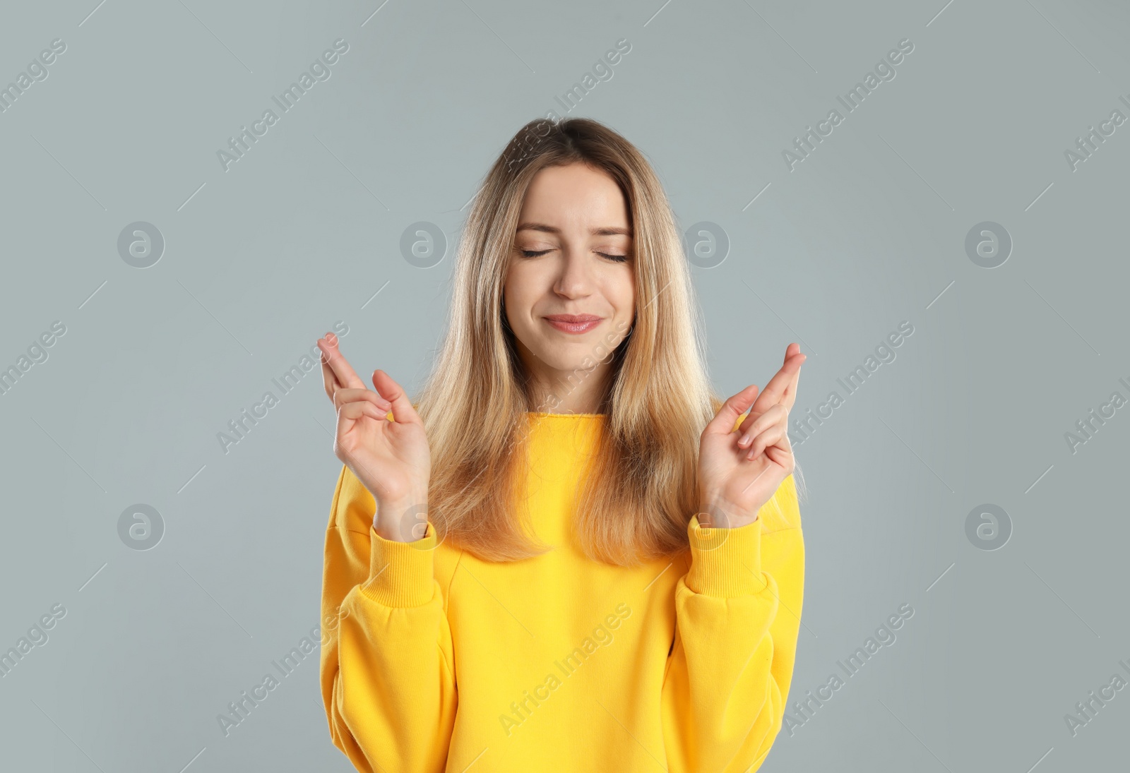 Photo of Woman with crossed fingers on light grey background. Superstition concept