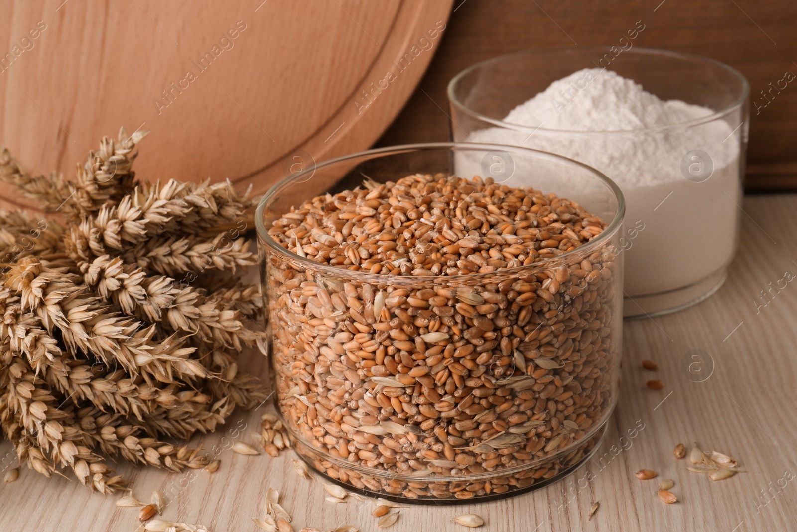 Photo of Wheat grains in bowl, spikes and flour on wooden table