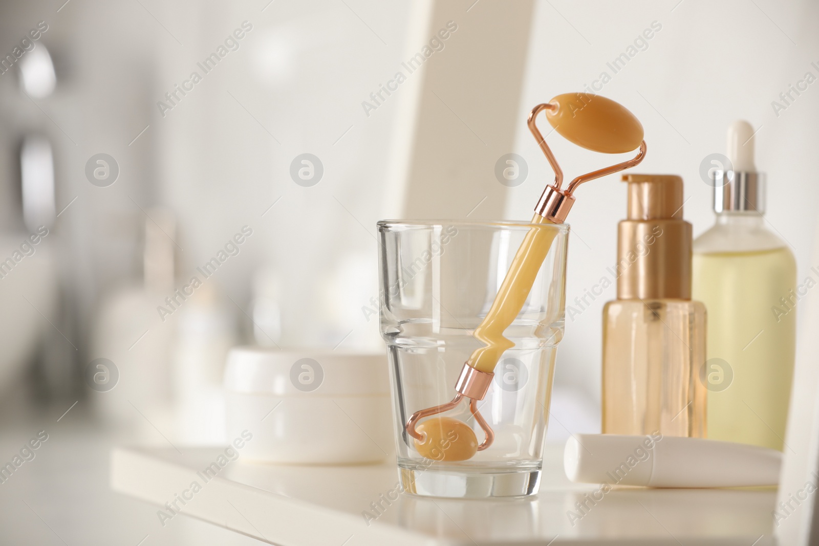 Photo of Natural face roller and cosmetic products on shelving unit in bathroom, closeup. Space for text