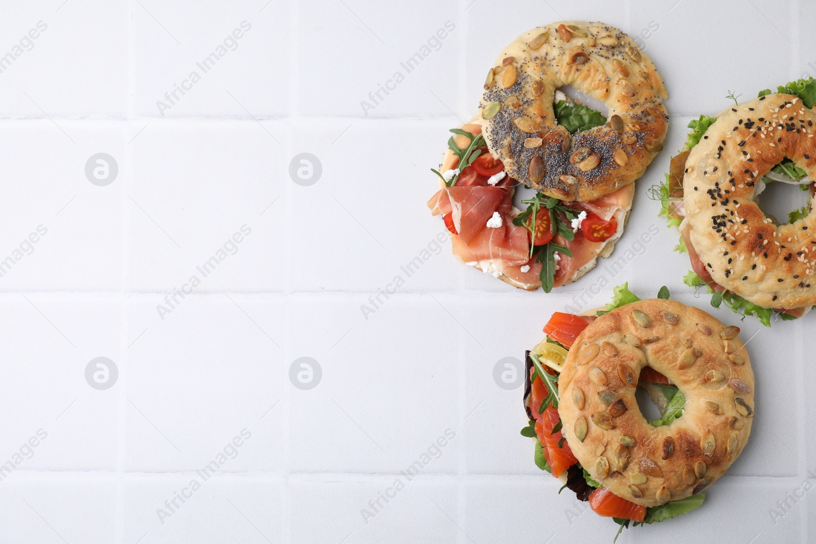 Photo of Tasty bagel sandwiches on white tiled table, flat lay. Space for text