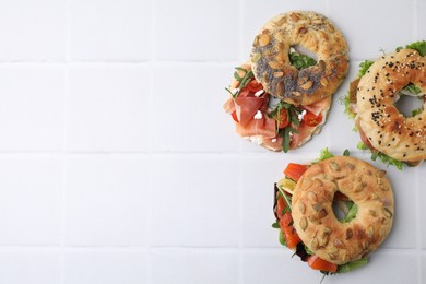 Tasty bagel sandwiches on white tiled table, flat lay. Space for text