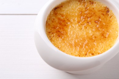 Photo of Delicious creme brulee in bowl on white wooden table, closeup