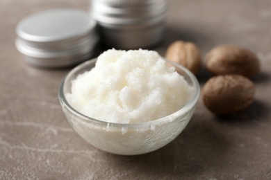 Shea butter in bowl and nuts on grey background, closeup