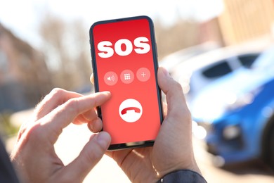 Image of Man holding smartphone with emergency call SOS on screen outdoors, closeup