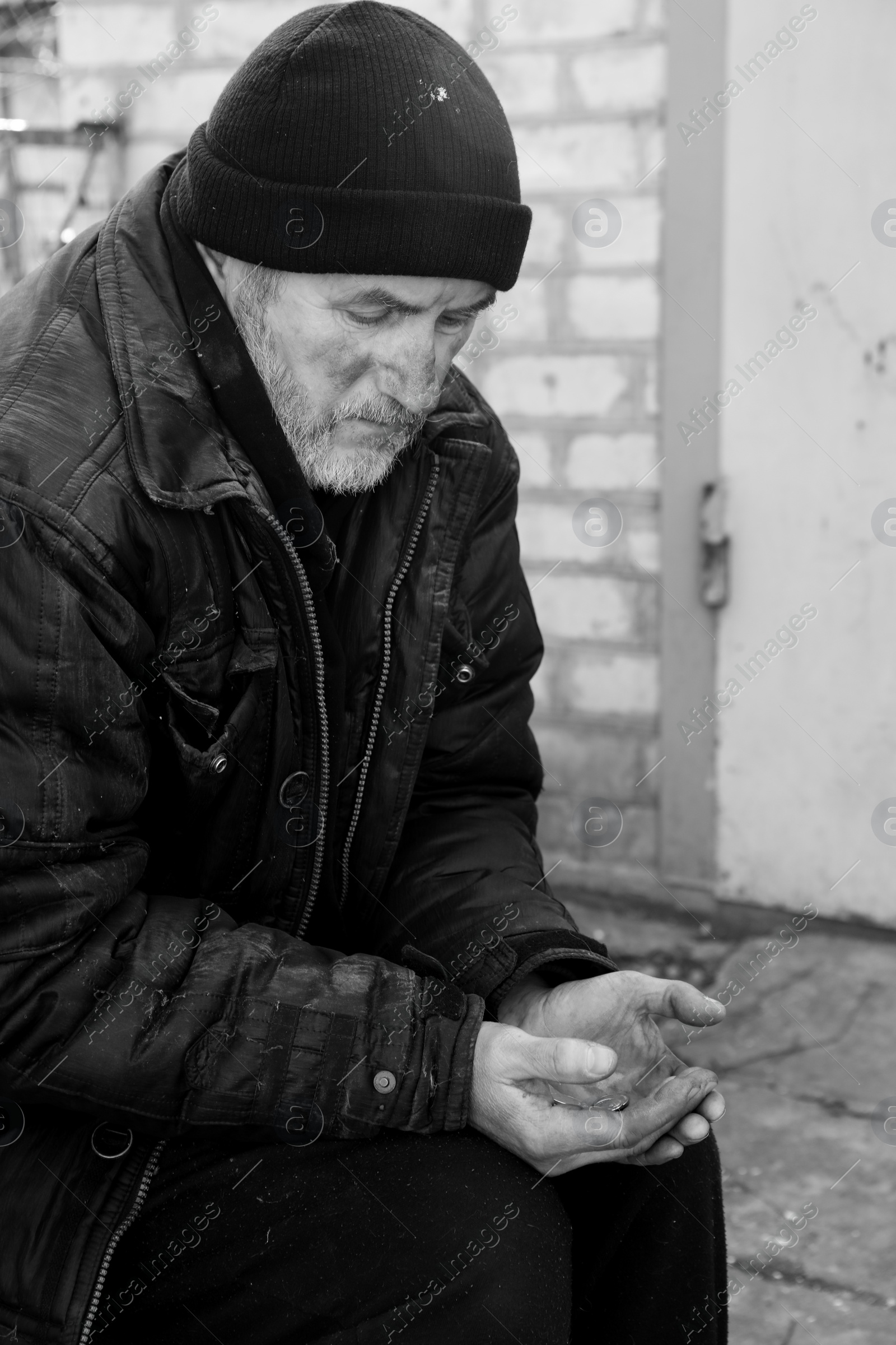 Photo of Poor homeless senior man holding coins outdoors. Black and white effect