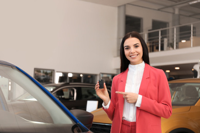 Young saleswoman with key near car in dealership