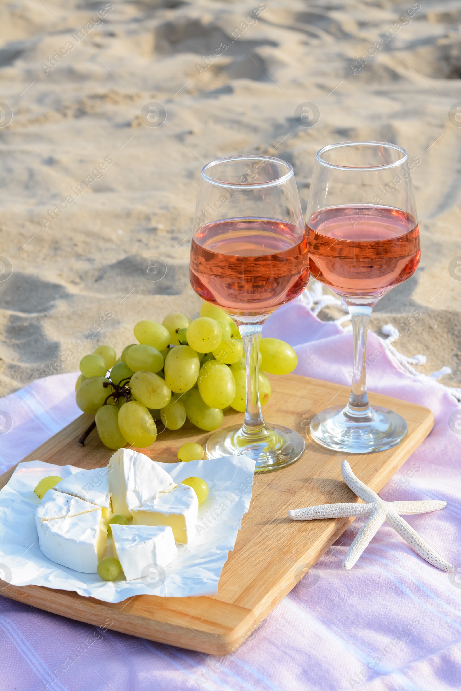 Photo of Glasses with rose wine and snacks for beach picnic on sand outdoors