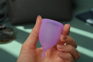 Photo of Woman holding violet menstrual cup on blurred background, closeup