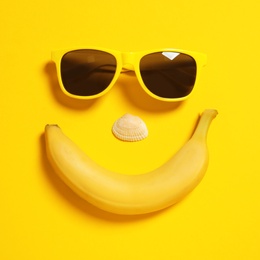 Photo of Funny face of sunglasses, banana and seashell on color background, top view. Beach accessories