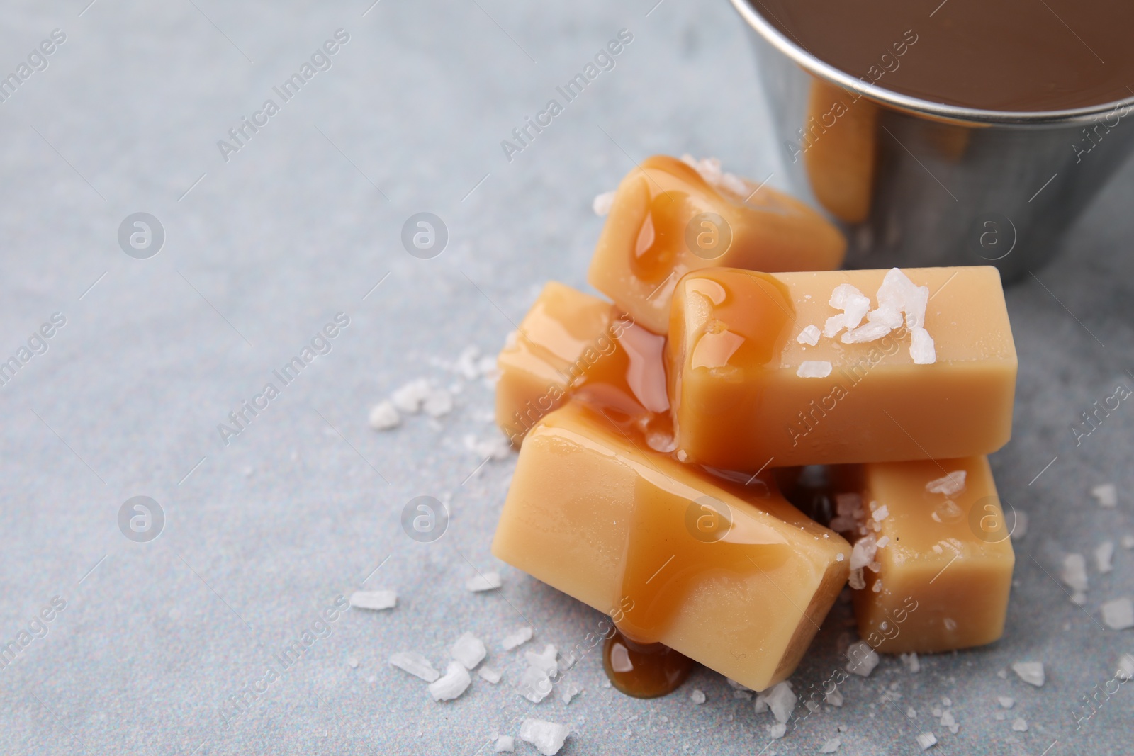 Photo of Yummy caramel candies, sauce and sea salt on grey table, closeup. Space for text