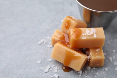 Yummy caramel candies, sauce and sea salt on grey table, closeup. Space for text