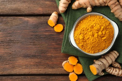 Bowl with aromatic turmeric powder and cut roots on wooden table, flat lay. Space for text