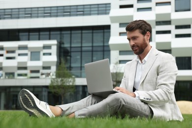 Handsome businessman with laptop on green grass outdoors