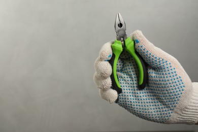 Man with combination pliers on grey background, closeup. Space for text