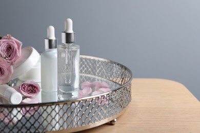 Bottles of cosmetic serum and beautiful flowers on wooden table against light gray background, space for text