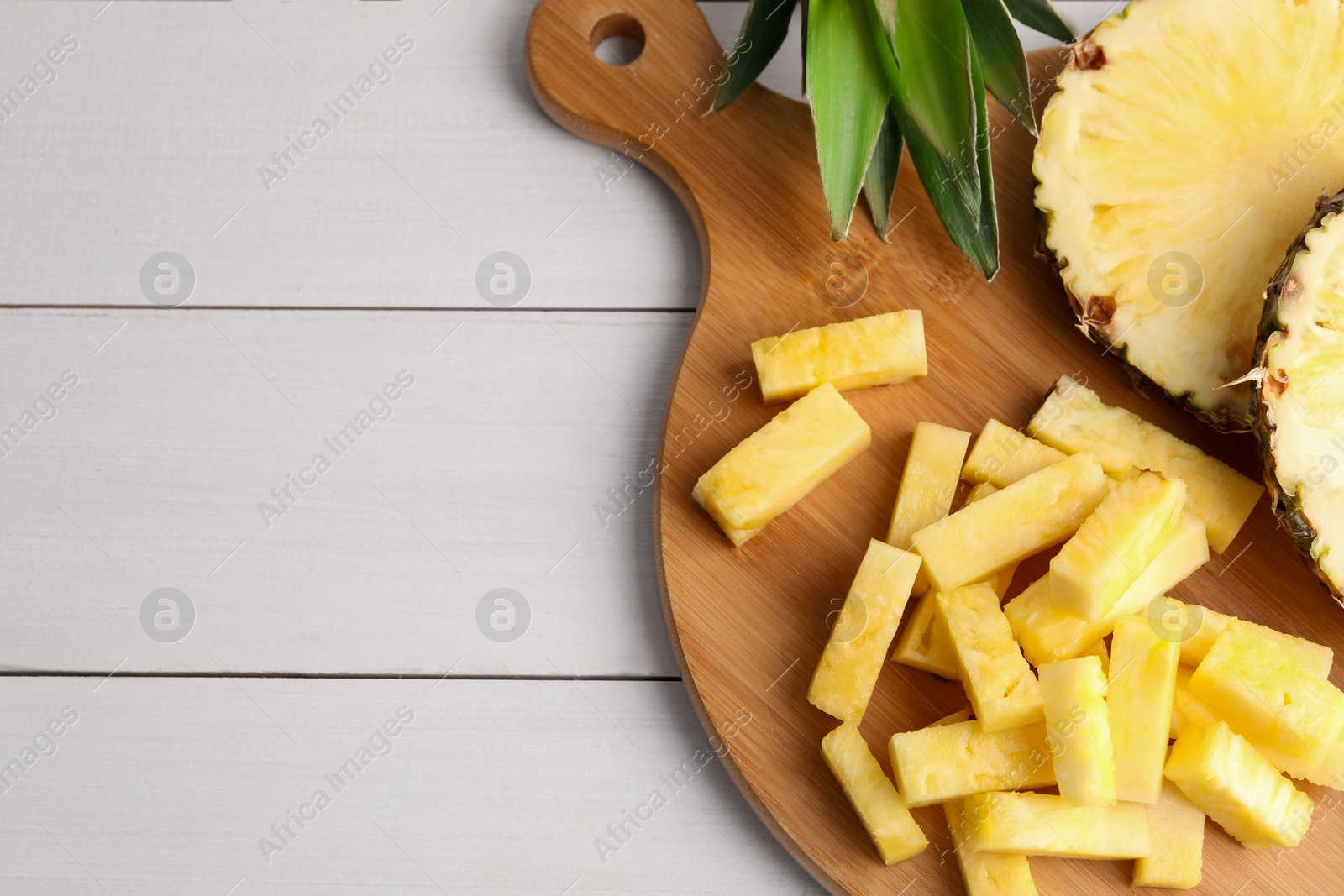 Photo of Pieces of tasty ripe pineapple on white wooden table, top view. Space for text