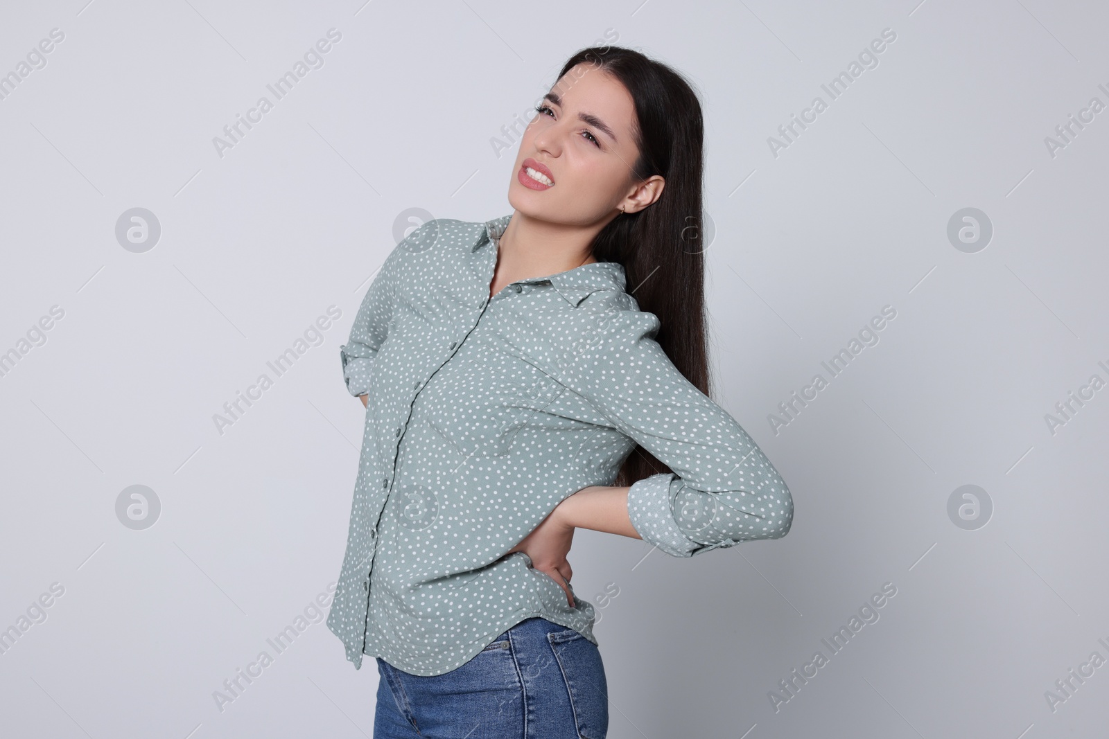 Photo of Young woman suffering from pain in back on light grey background. Arthritis symptoms