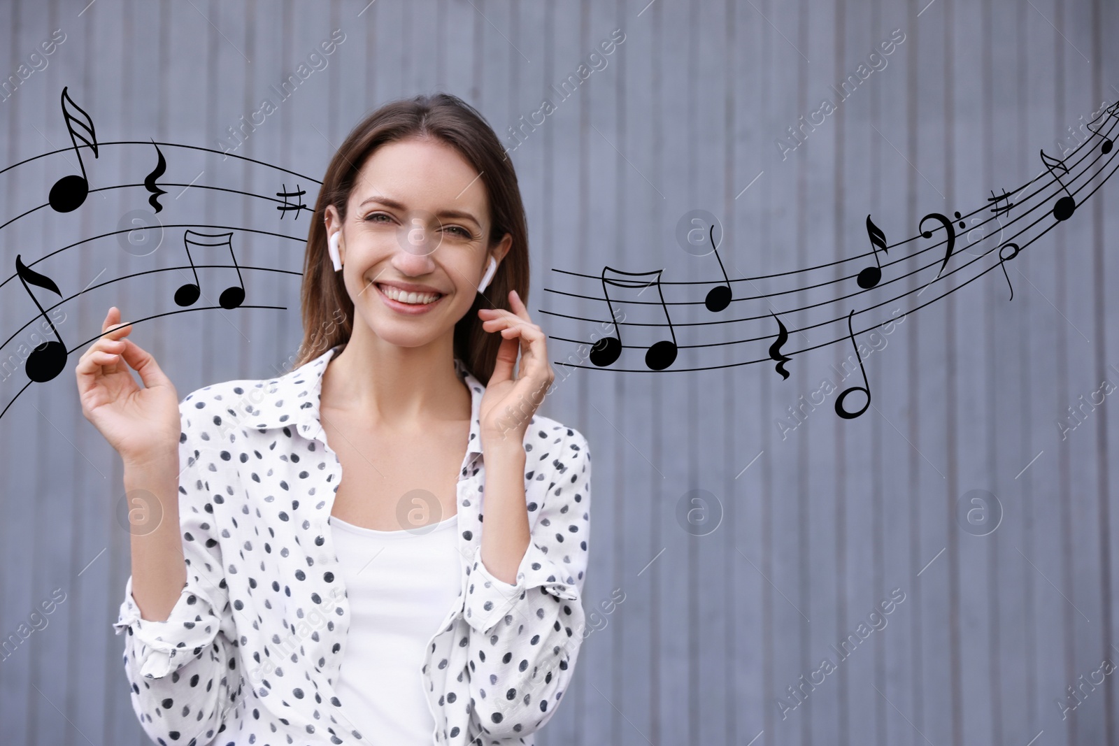 Image of Young woman listening to music with wireless headphones near grey wall