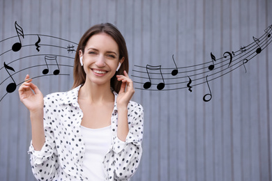 Young woman listening to music with wireless headphones near grey wall