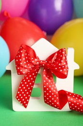 Wooden house model with red bow and balloons on green background. Housewarming party