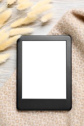 Modern e-book reader near dried flowers on white wooden table, flat lay