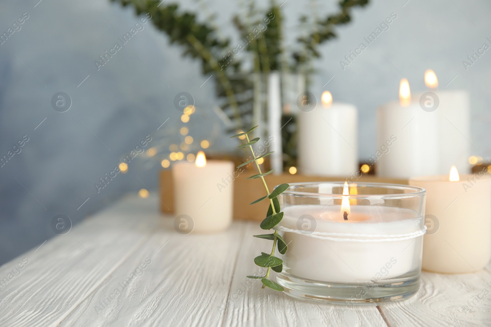 Photo of Burning aromatic candle and eucalyptus branch on table. Space for text