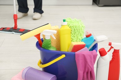 Photo of Different cleaning supplies in bucket and man mopping floor, selective focus