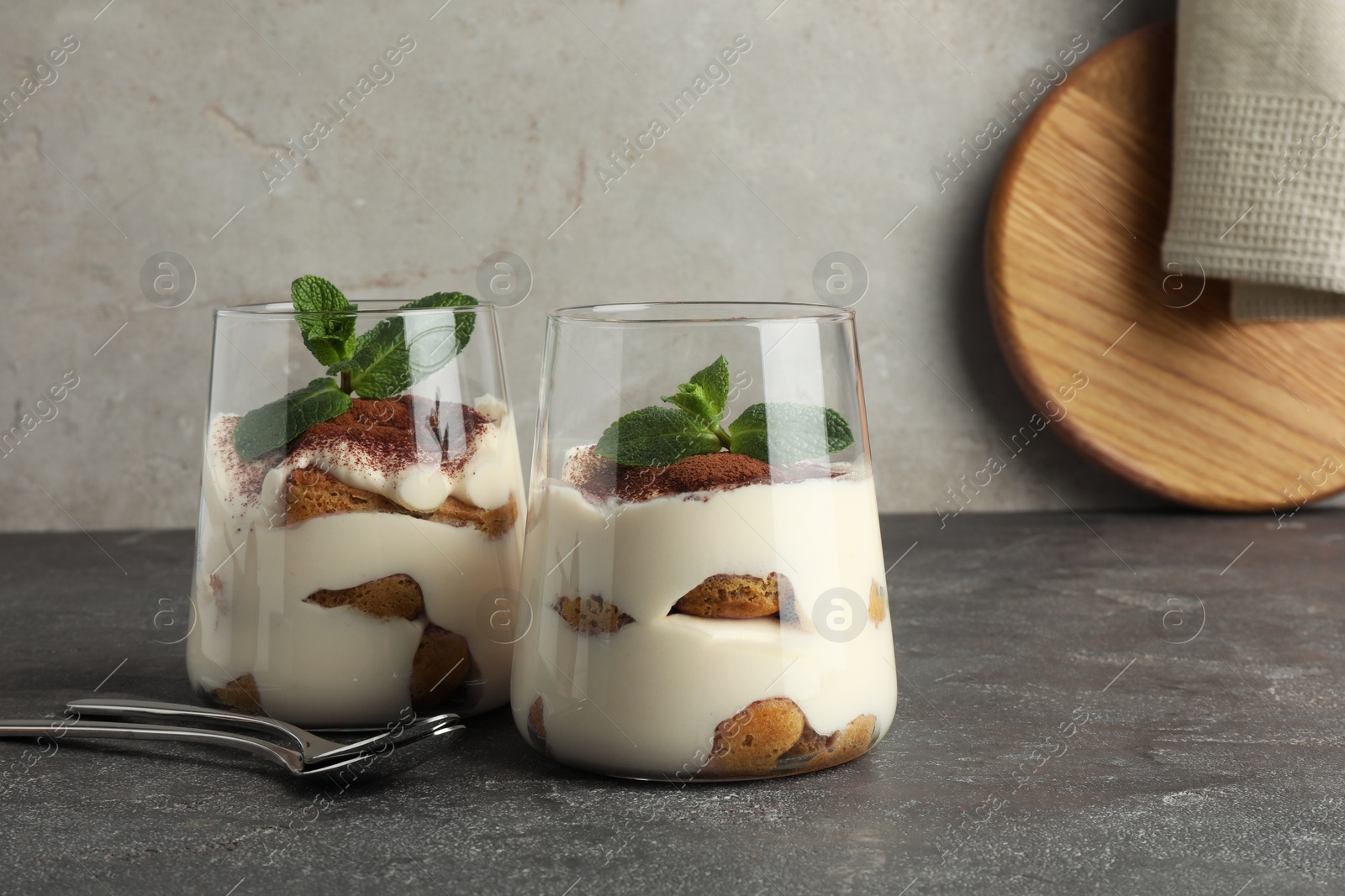 Photo of Delicious tiramisu with mint in glasses on grey table