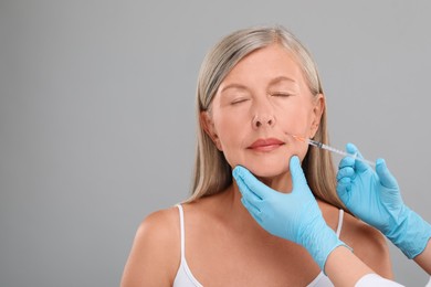 Photo of Doctor giving facial injection to senior woman on light grey background, closeup and space for text. Cosmetic surgery