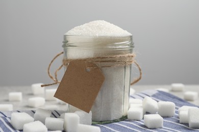 Glass jar of granulated sugar and cubes on table