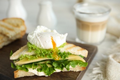 Photo of Delicious sandwich with vegetables and poached egg on board, closeup