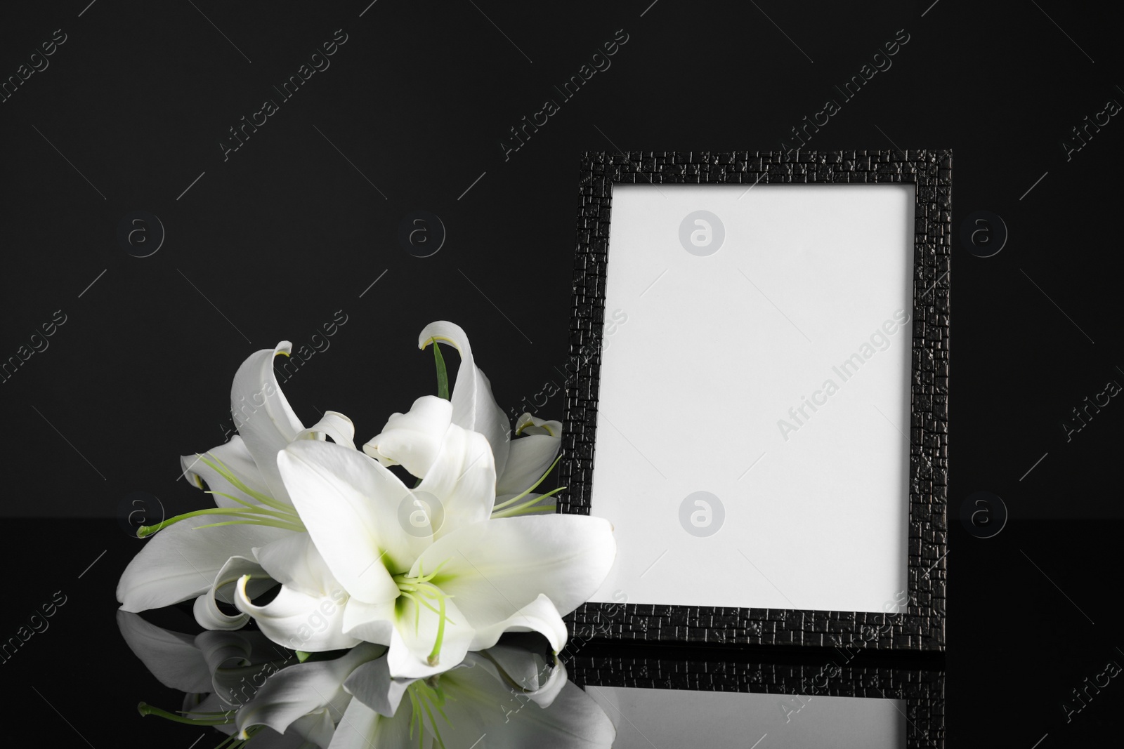 Photo of Funeral photo frame and white lilies on black table against dark background. Space for design