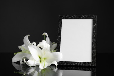 Photo of Funeral photo frame and white lilies on black table against dark background. Space for design