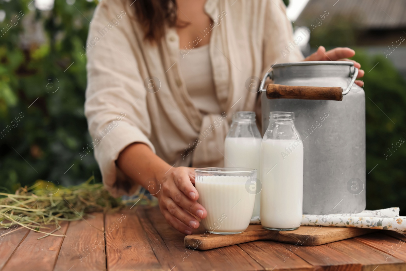 Photo of Woman taking glass with fresh milk at wooden table outdoors, closeup