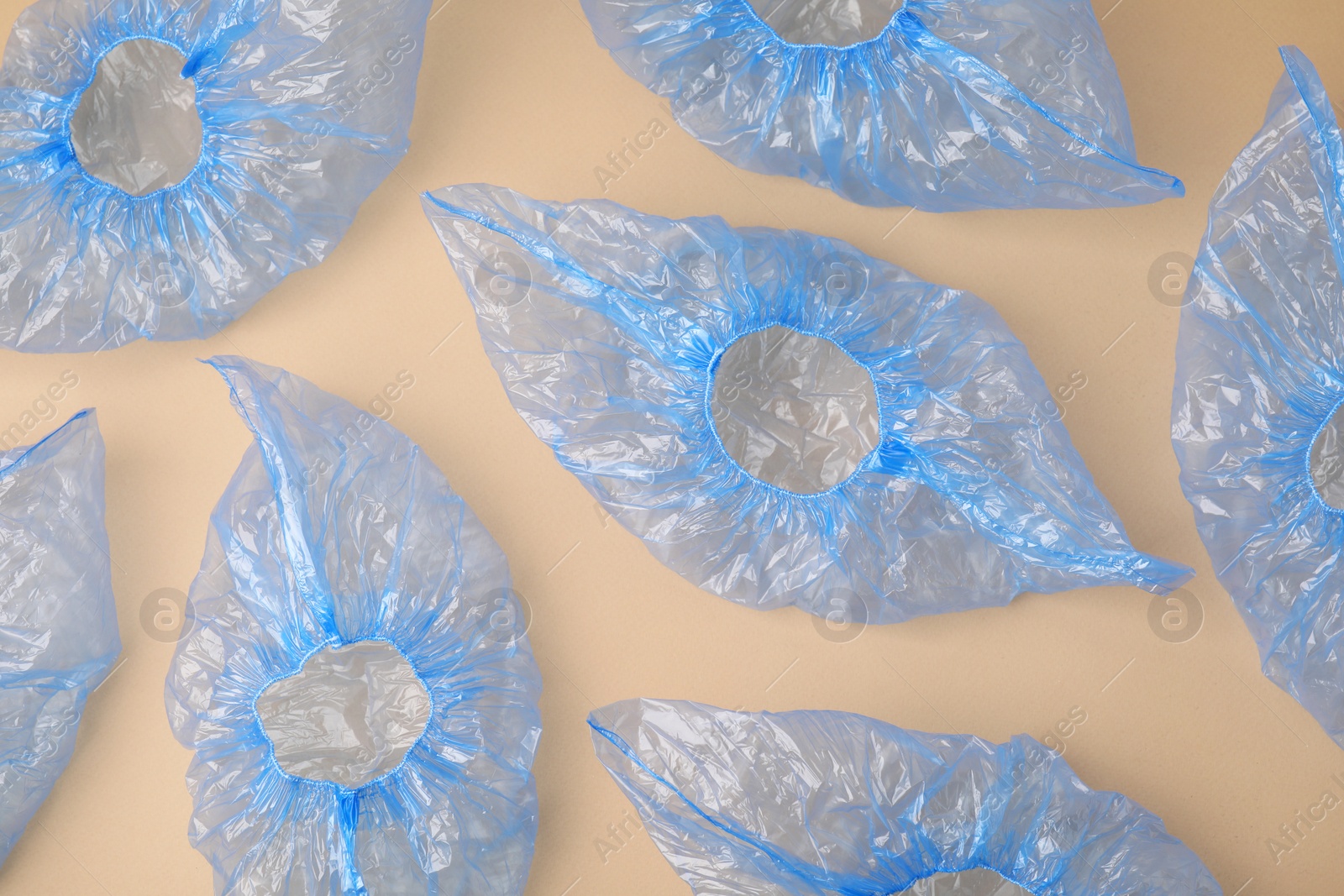 Photo of Blue medical shoe covers on beige background, flat lay