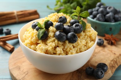 Photo of Tasty millet porridge with blueberries and mint in bowl on light blue wooden table, closeup