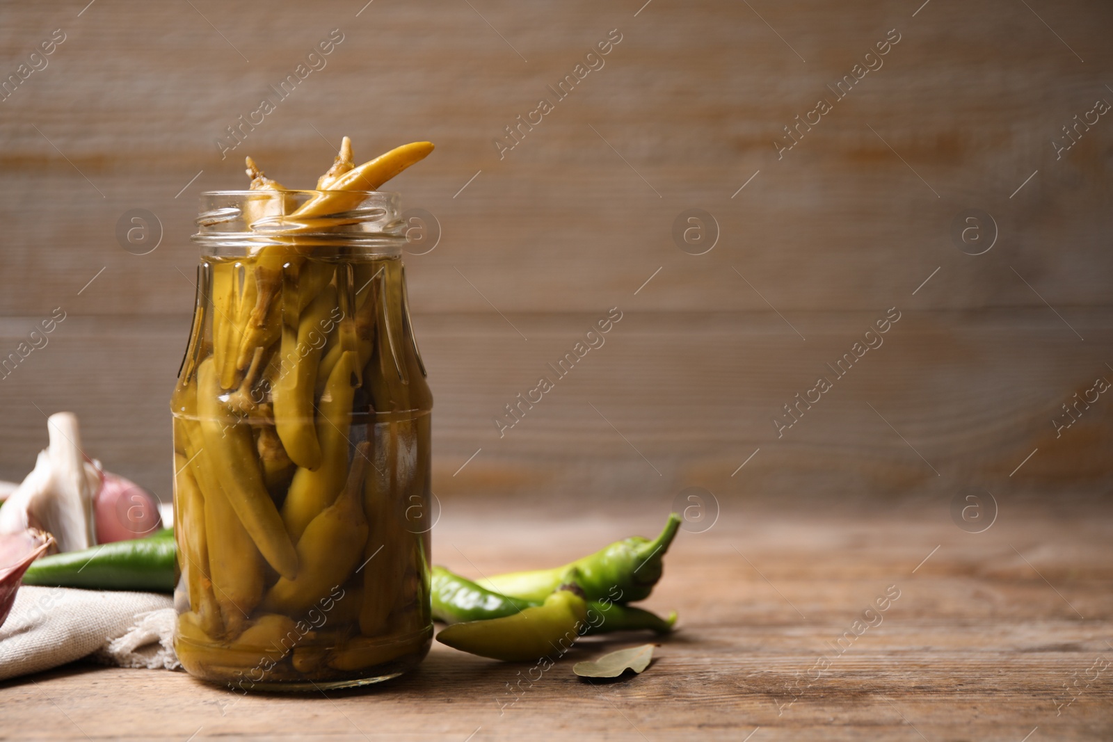 Photo of Glass jar with pickled peppers on wooden table. Space for text