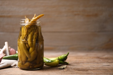 Glass jar with pickled peppers on wooden table. Space for text