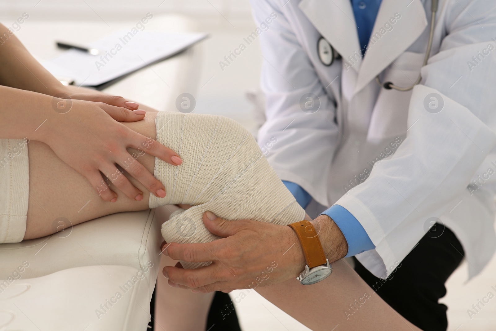 Photo of Orthopedist applying bandage onto patient's knee in clinic, closeup