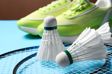 Feather badminton shuttlecocks, rackets and sneakers on light blue background, closeup