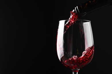 Photo of Pouring red wine into glass against black background, closeup. Space for text