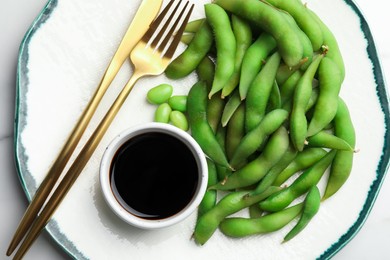 Photo of Green edamame beans in pods served with soy sauce on plate, top view