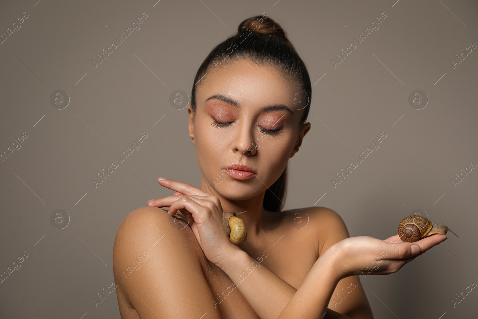 Photo of Beautiful young woman with snails on her hands against beige background